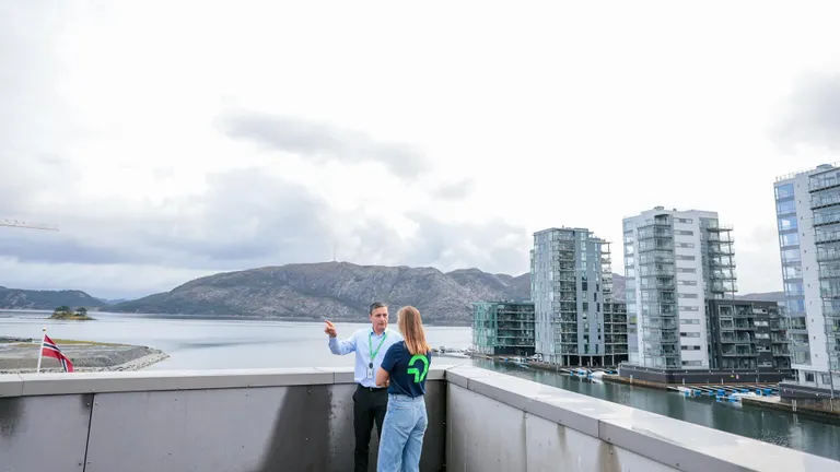 Two OMV employees talking on a rooftop with fjord, mountains, and modern buildings in the background in Norway.